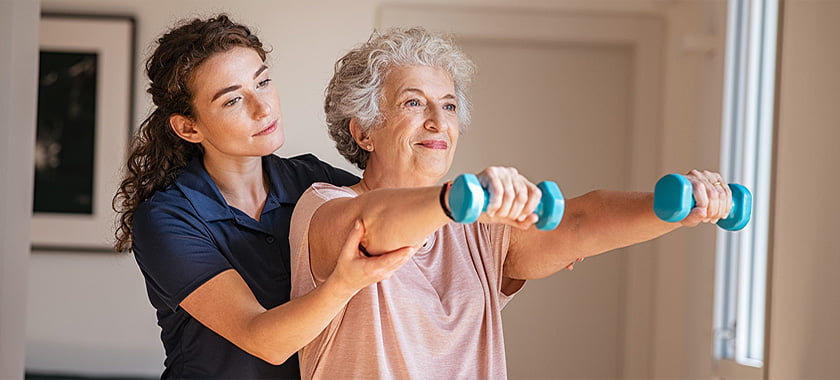 A woman helping an older person with some exercise equipment